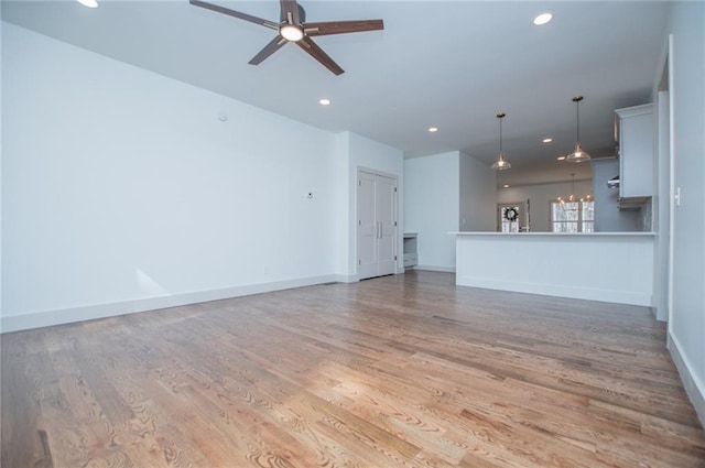 unfurnished living room with light wood finished floors, recessed lighting, baseboards, and ceiling fan with notable chandelier