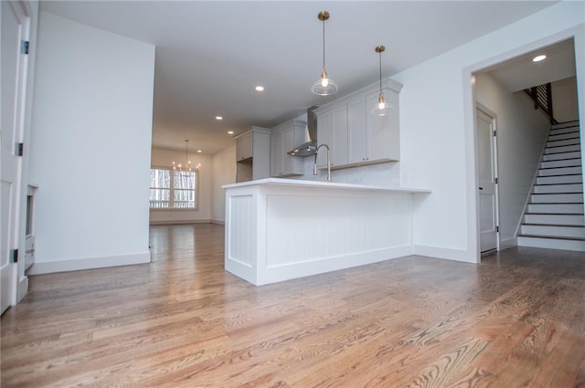 kitchen featuring light wood-type flooring, wall chimney exhaust hood, light countertops, and recessed lighting