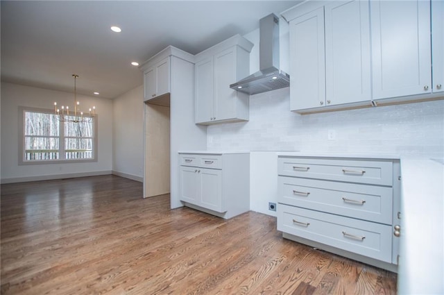 kitchen with a notable chandelier, recessed lighting, wall chimney range hood, light wood-type flooring, and tasteful backsplash