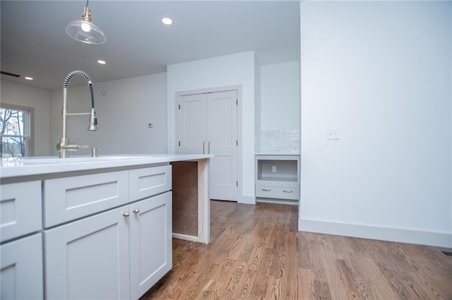 kitchen with wood finished floors, decorative light fixtures, light countertops, a sink, and recessed lighting