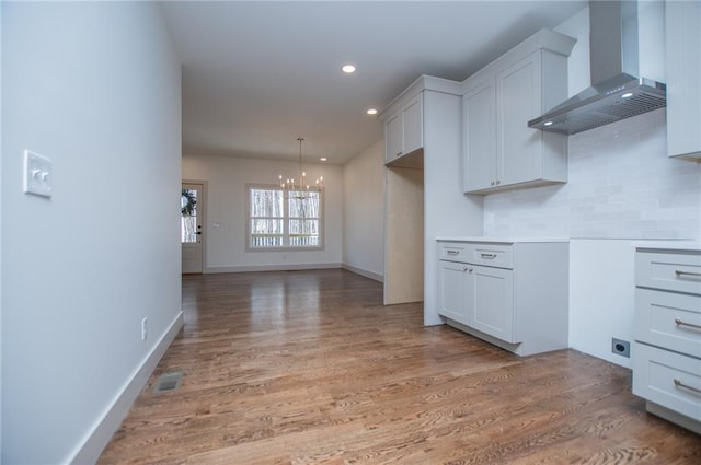 kitchen featuring recessed lighting, light wood-type flooring, backsplash, wall chimney exhaust hood, and an inviting chandelier