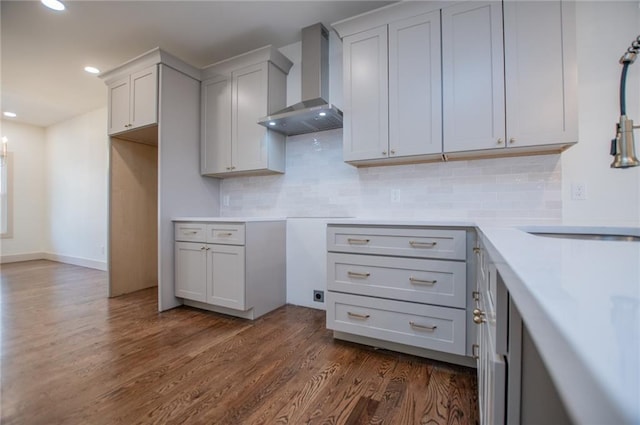 kitchen with backsplash, light countertops, dark wood finished floors, and wall chimney range hood