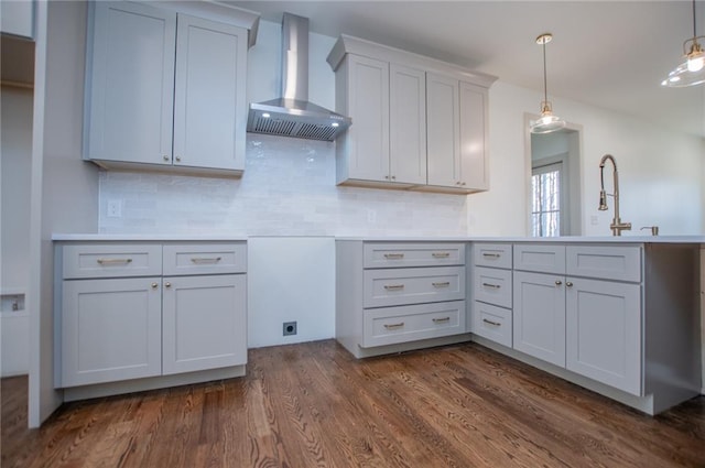 kitchen with a peninsula, wall chimney range hood, tasteful backsplash, dark wood finished floors, and pendant lighting