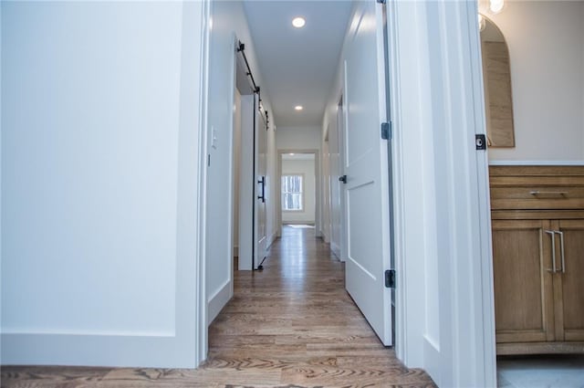 hallway featuring recessed lighting, light wood finished floors, and a barn door