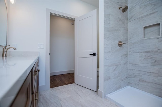 full bath with tiled shower, vanity, and baseboards