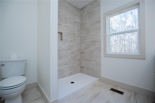 full bathroom with toilet, tiled shower, visible vents, and baseboards