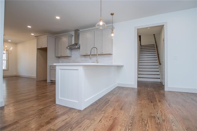 kitchen with light countertops, a peninsula, wall chimney exhaust hood, and wood finished floors