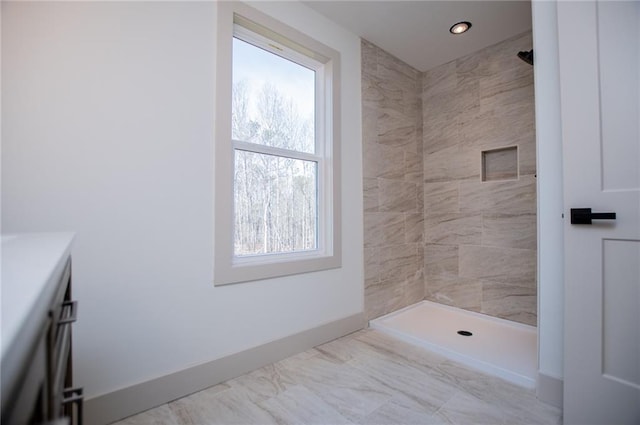 bathroom featuring baseboards, a tile shower, and vanity