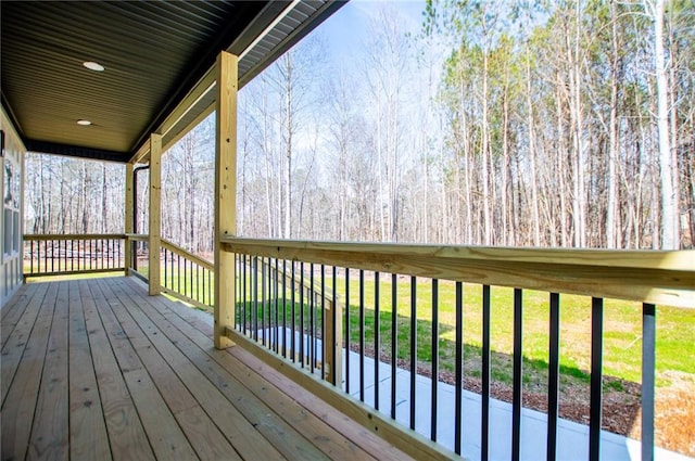 wooden terrace featuring a lawn and a forest view