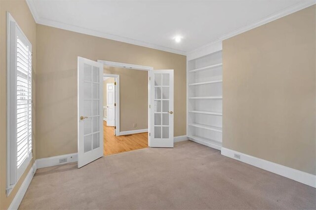 unfurnished room featuring light carpet, french doors, crown molding, and built in features