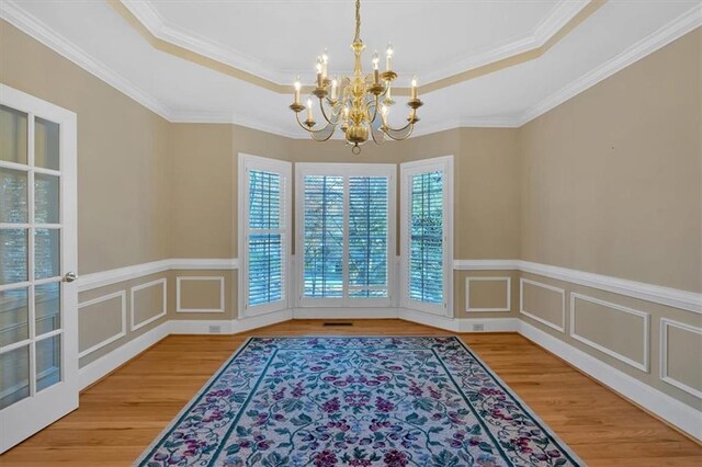 unfurnished dining area featuring a raised ceiling, wood-type flooring, ornamental molding, and an inviting chandelier