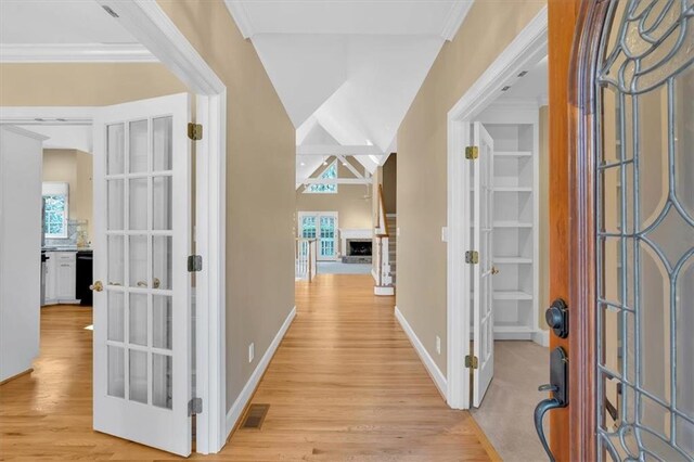 hall featuring french doors, light hardwood / wood-style floors, lofted ceiling, and ornamental molding