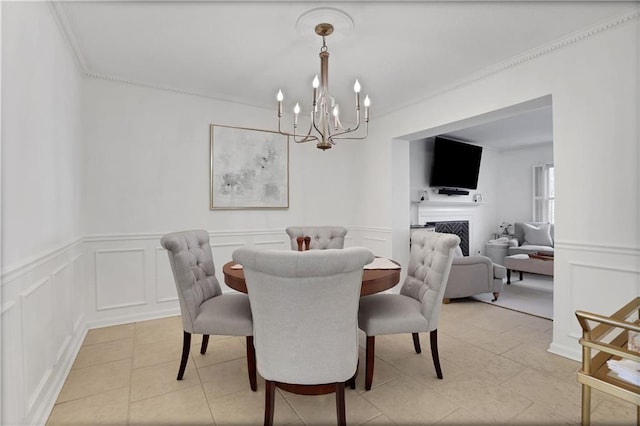 dining area featuring crown molding, a chandelier, a fireplace, light tile patterned flooring, and a decorative wall