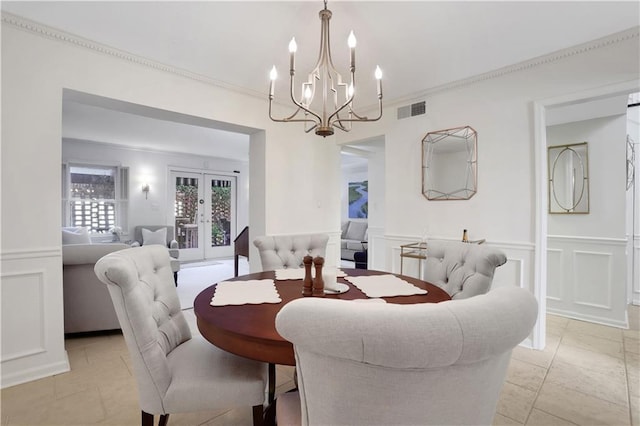 dining room featuring visible vents, french doors, crown molding, a decorative wall, and a chandelier