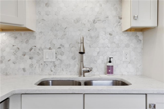 kitchen featuring white cabinetry, light stone counters, backsplash, and a sink