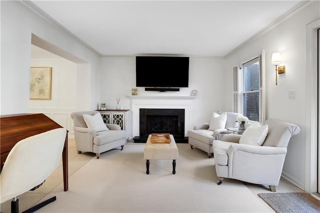 living area with wainscoting, a decorative wall, a fireplace with raised hearth, and crown molding