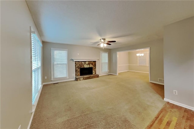 unfurnished living room featuring visible vents, baseboards, carpet flooring, a fireplace, and ceiling fan with notable chandelier