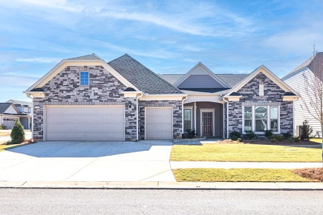 craftsman-style home featuring a front yard, driveway, roof with shingles, stone siding, and a garage