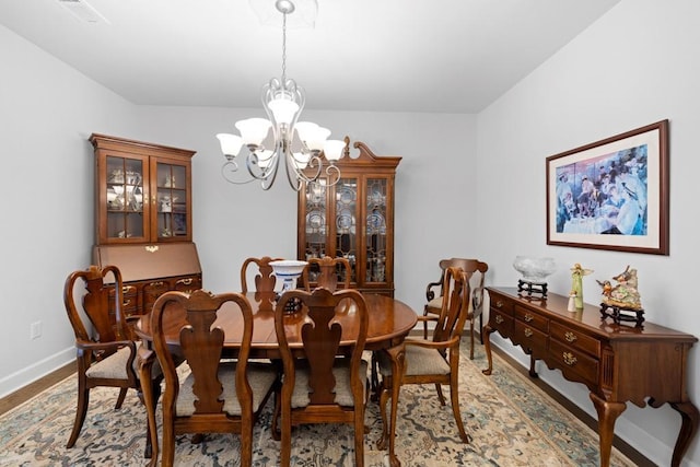 dining space with wood finished floors, a notable chandelier, visible vents, and baseboards