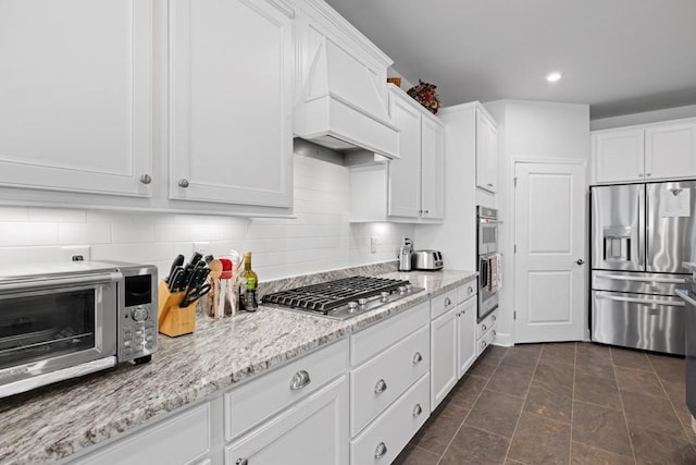 kitchen with tasteful backsplash, light stone countertops, appliances with stainless steel finishes, custom exhaust hood, and white cabinetry