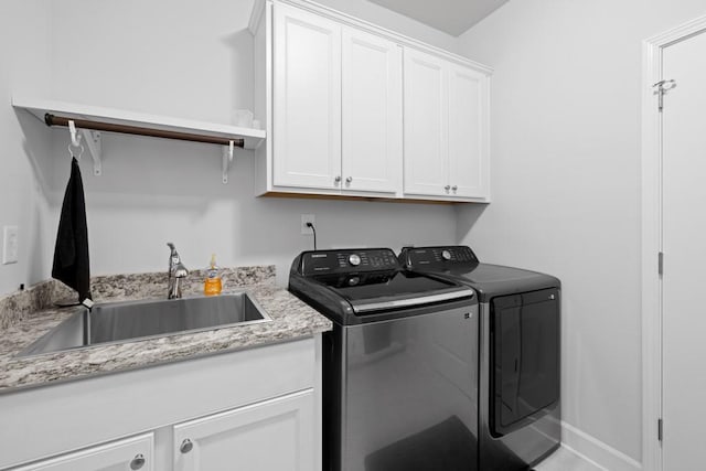 clothes washing area with a sink, baseboards, cabinet space, and washer and clothes dryer