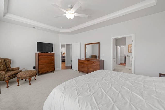 bedroom featuring light carpet, a ceiling fan, ensuite bathroom, and a tray ceiling