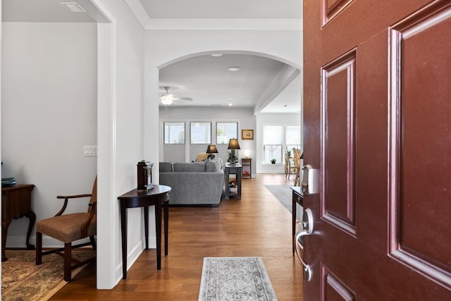 foyer with arched walkways, crown molding, a ceiling fan, and wood finished floors