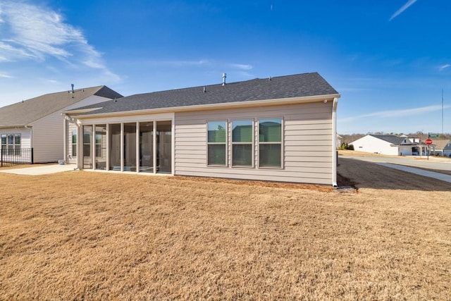 back of house featuring a lawn, a sunroom, and roof with shingles