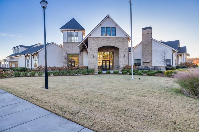 view of front facade featuring a standing seam roof, a front yard, metal roof, brick siding, and a chimney