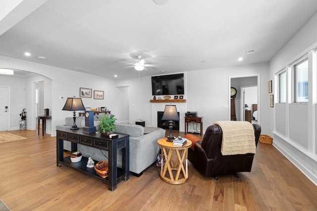 living area with a brick fireplace, recessed lighting, wood finished floors, and arched walkways