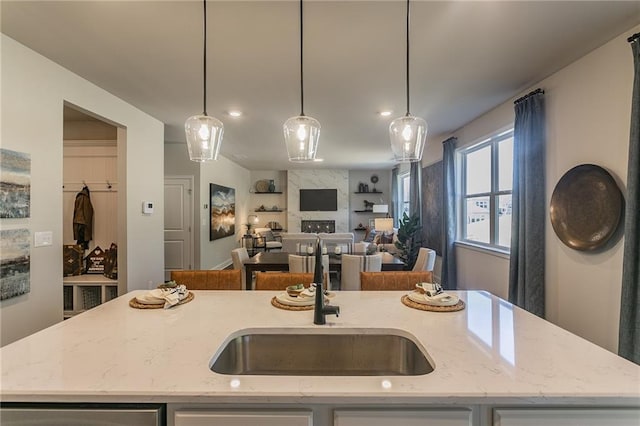 kitchen featuring light stone counters, a center island with sink, hanging light fixtures, and a sink