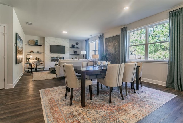 dining room with dark wood finished floors, a high end fireplace, visible vents, and baseboards