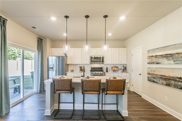 kitchen featuring white cabinets, appliances with stainless steel finishes, a sink, a kitchen island with sink, and backsplash