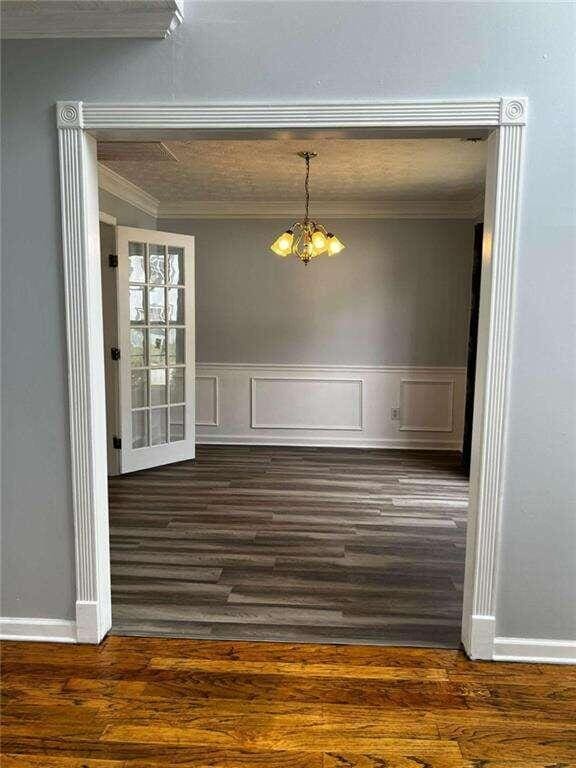 unfurnished dining area featuring dark hardwood / wood-style flooring, a notable chandelier, and ornamental molding