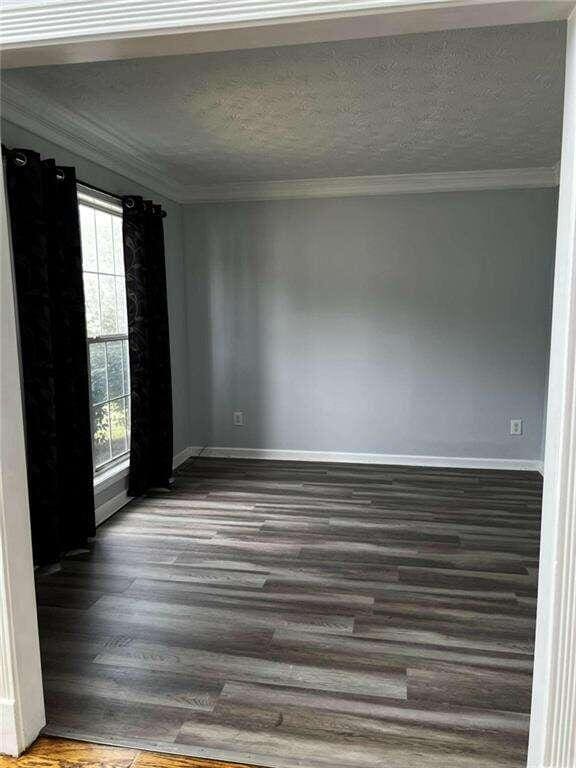 unfurnished room with dark wood-type flooring, a textured ceiling, and ornamental molding