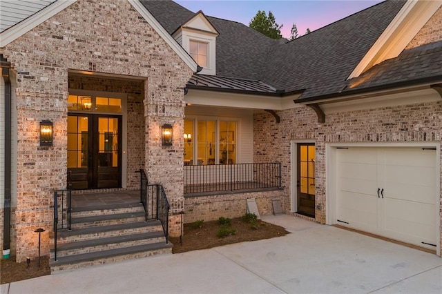 view of exterior entry featuring french doors, brick siding, driveway, and a standing seam roof