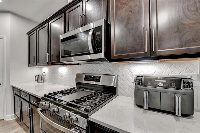 kitchen featuring light stone counters, light wood-style flooring, dark brown cabinets, appliances with stainless steel finishes, and decorative backsplash