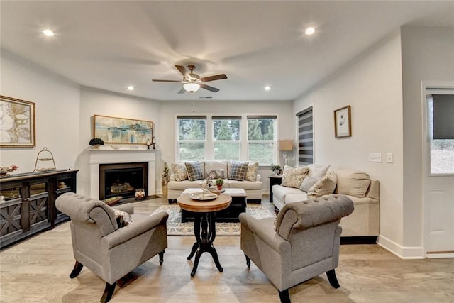 living room featuring baseboards, a glass covered fireplace, ceiling fan, light wood-style flooring, and recessed lighting