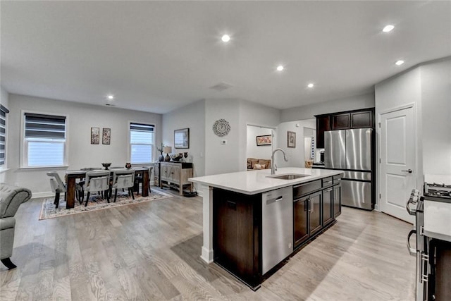 kitchen with a kitchen island with sink, a sink, light countertops, appliances with stainless steel finishes, and light wood-type flooring