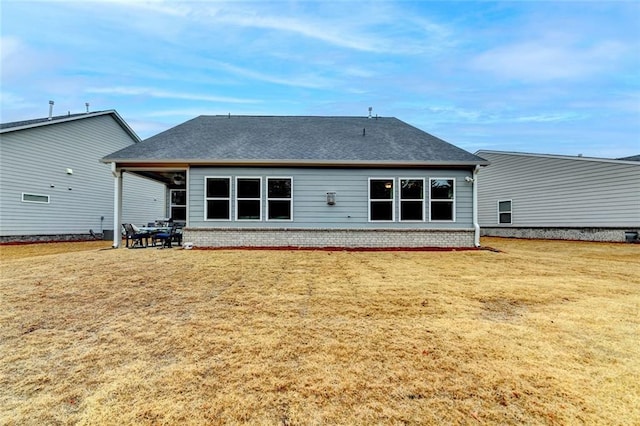 back of house with a yard, roof with shingles, and brick siding