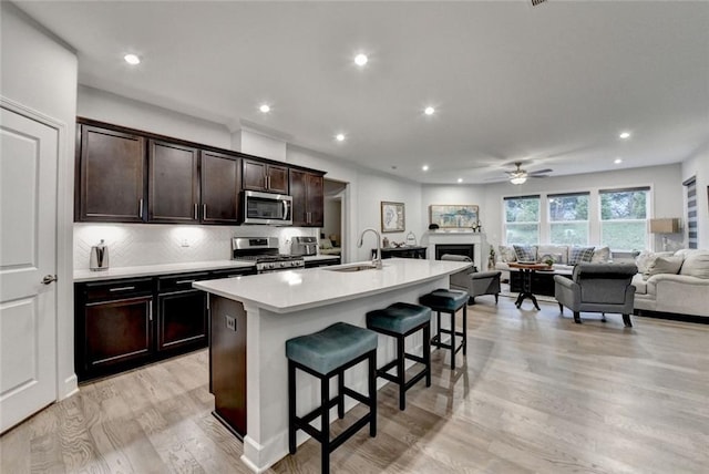 kitchen with a fireplace, a breakfast bar area, appliances with stainless steel finishes, open floor plan, and a kitchen island with sink