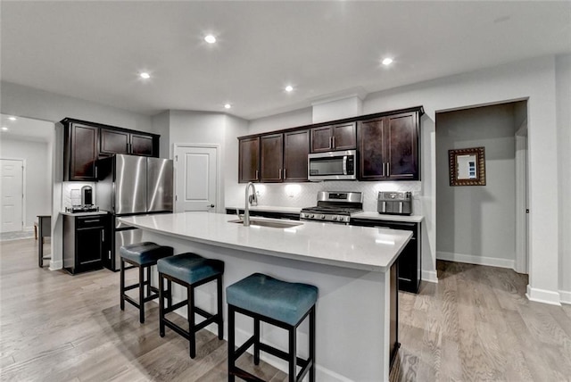 kitchen with a breakfast bar, a sink, appliances with stainless steel finishes, light wood finished floors, and tasteful backsplash