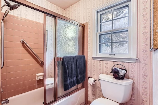 bathroom featuring toilet and shower / bath combination with glass door