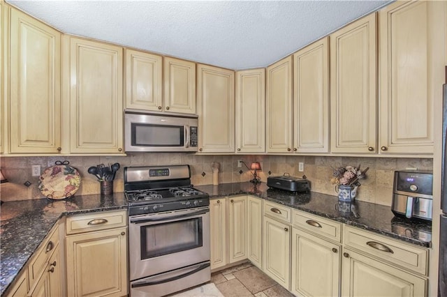 9760 Loblolly Ln, Roswell, GA 30075 - kitchen featuring appliances with stainless steel finishes, cream cabinets, dark stone counters, and a textured ceiling