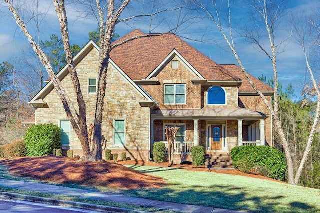 craftsman-style house with a shingled roof, stone siding, a porch, a front lawn, and brick siding