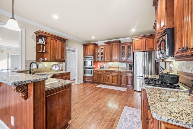 kitchen with appliances with stainless steel finishes, pendant lighting, brown cabinets, and glass insert cabinets