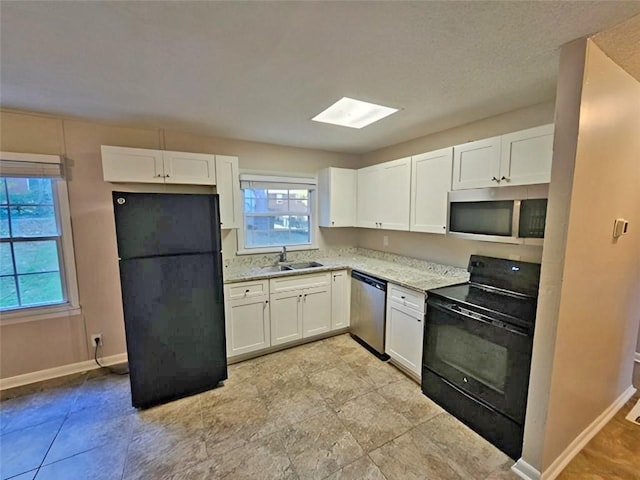 kitchen with sink, white cabinetry, a skylight, light stone countertops, and black appliances