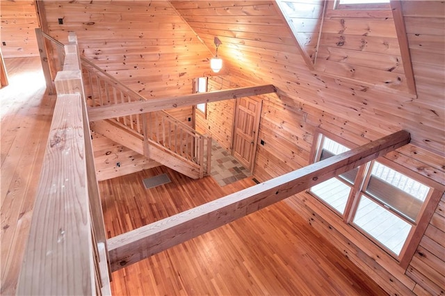 staircase featuring wood walls, high vaulted ceiling, and light wood-type flooring