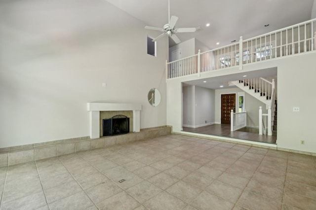 unfurnished living room featuring a ceiling fan, a high ceiling, a tile fireplace, stairway, and tile patterned floors