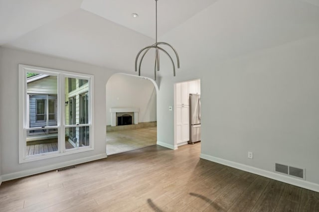 unfurnished dining area featuring wood finished floors, baseboards, arched walkways, and a fireplace with raised hearth